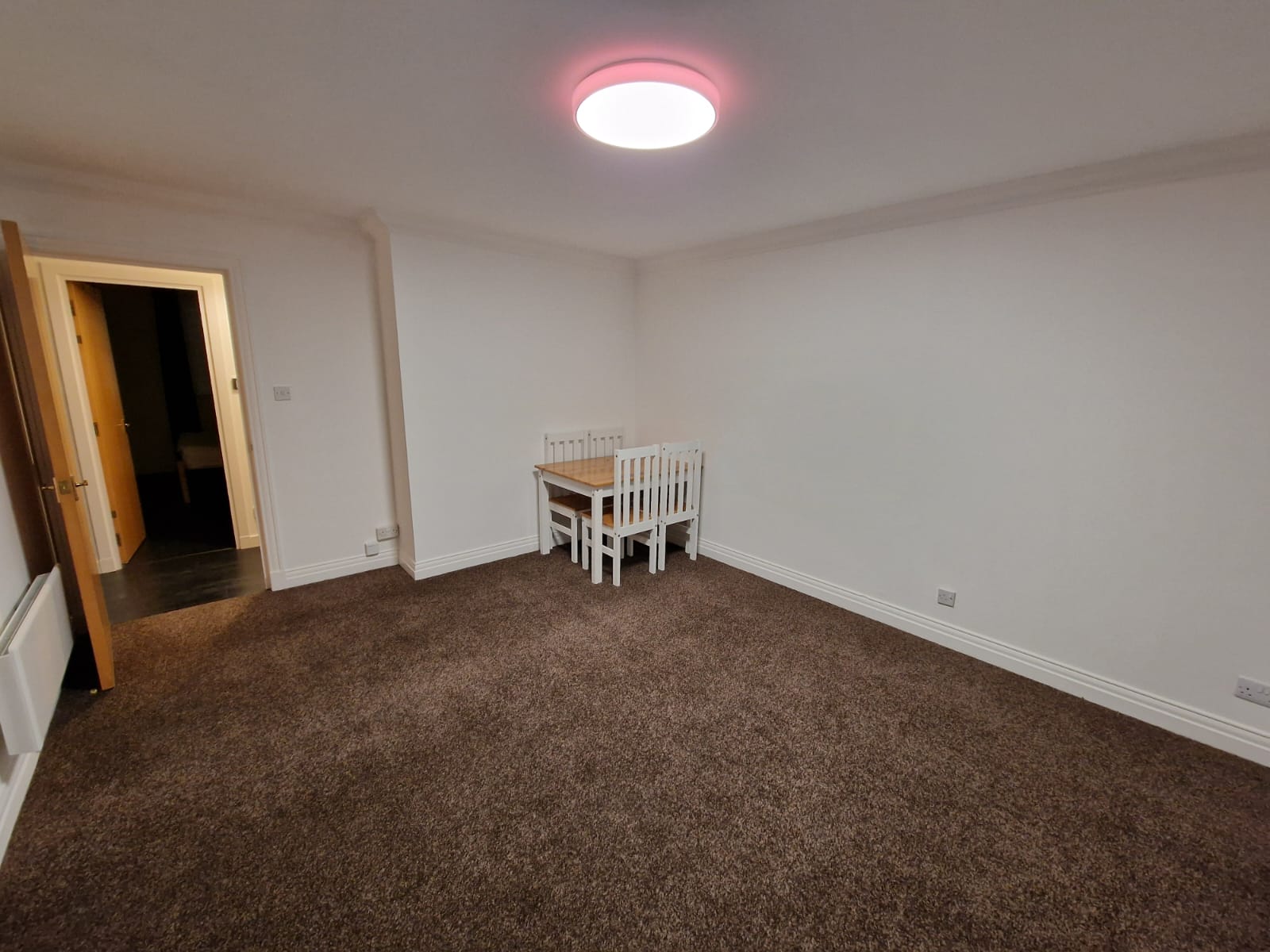 Living room with the dining table and chairs, electric heater and doorway to the hall