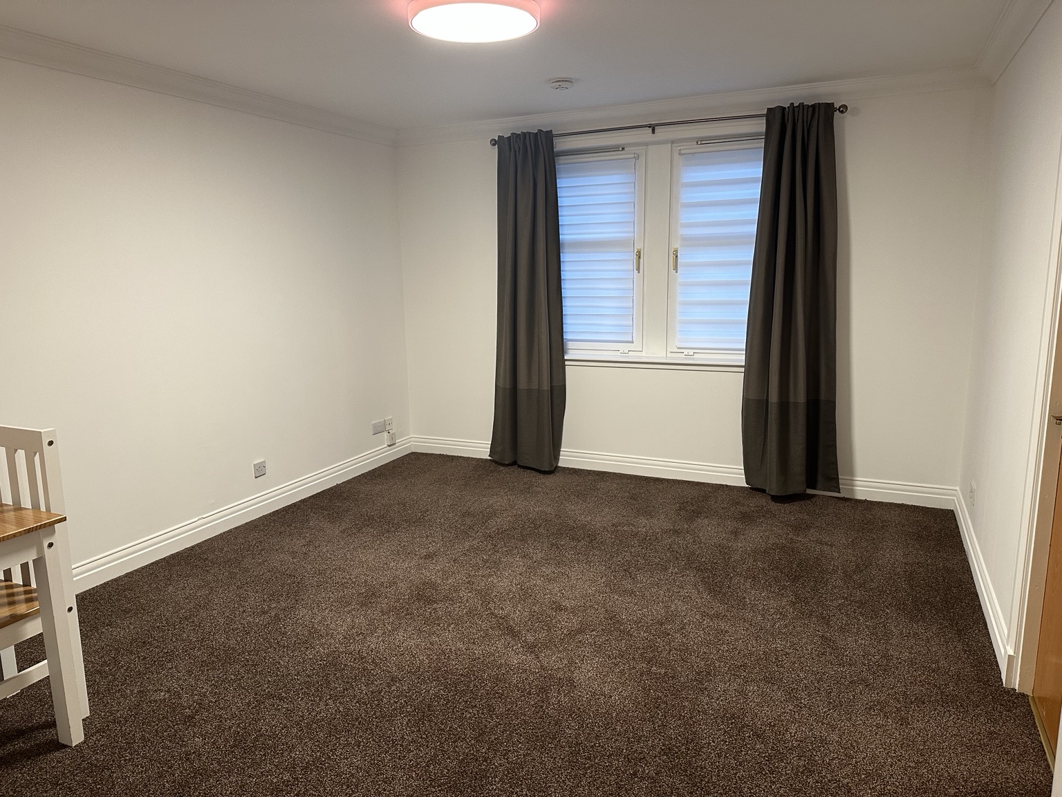 Living room facing the window, with open grey curtains, fitted blinds and brown carpet